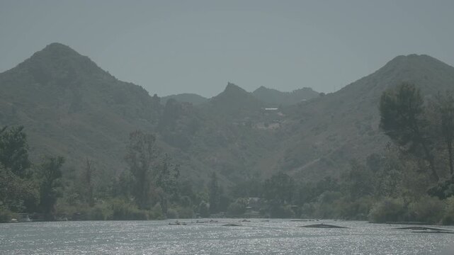 Mountain peaks and green trees above a wide riverbed in clear light
