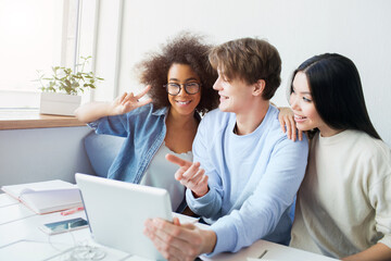 Fototapeta premium Nice picture of guy holding a tablet and girls talking with somebody using the tablet for that. Asian girl is leaning on the guy. Afro american girl is showing the piece symbol to the tablet's screen.