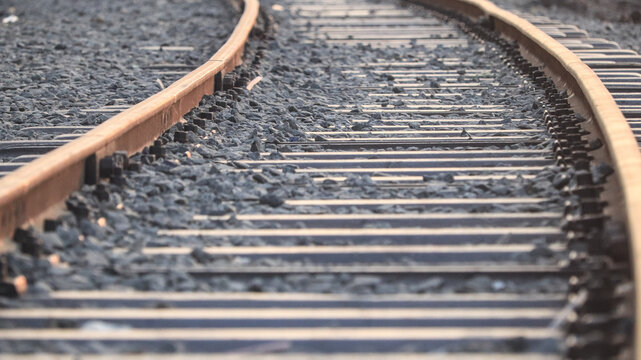 Rusty curved railway tracks with dark stone ballast in perspective view for industrial transport and travel concept