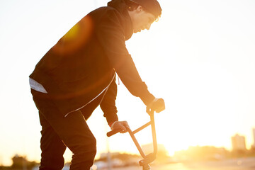 Naklejka premium Balance, city and sunset with man on bicycle for adrenaline, exercise or extreme sports outdoor. BMX, flare and training with bike rider on street in urban town for action, hobby or skill practice