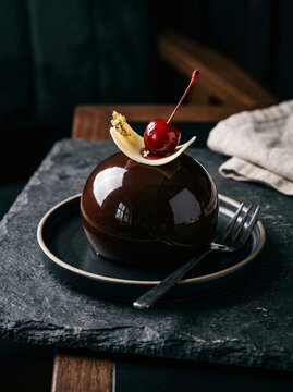 A gourmet chocolate dome dessert topped with a fresh cherry and white chocolate garnish.