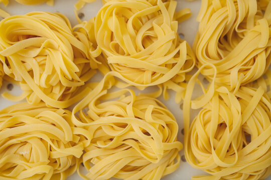 Overhead close-up of fresh fettuccine pasta nests with twisted golden strands and textured dough on light kitchen surface, arranged for cooking