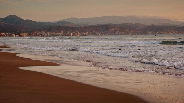 Gentle ocean waves rolling onto a sandy beach shore during a golden sunrise under soft cloudy sky.