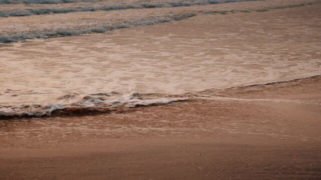 Close-up of soft sea foam washing over a sandy beach shoreline during golden sunrise light
