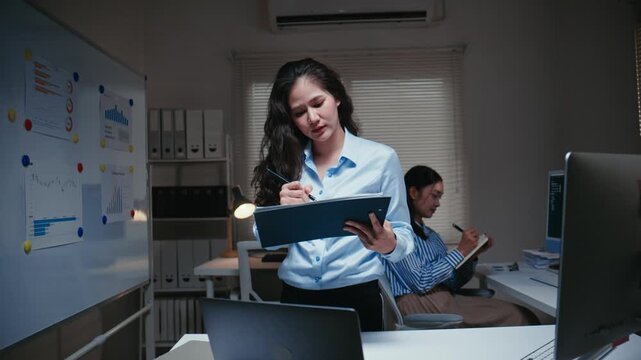 Young businesswoman writing notes in a folder while working late at night in the office