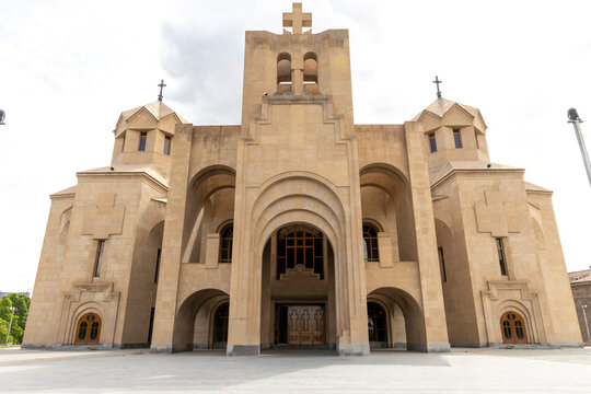 Front facade of Saint Gregory the Illuminator Cathedral with tall bell tower crosses twin turrets and arched wooden doors beneath a cloudy sky, Yerevan, Armenia