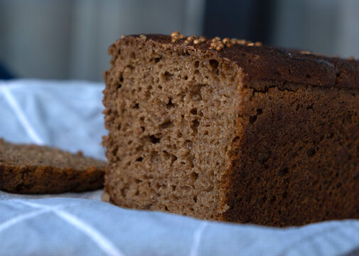 Traditional Borodinsky sourdough rye bread loaf with coriander seeds and a cut slice on a linen napkin.