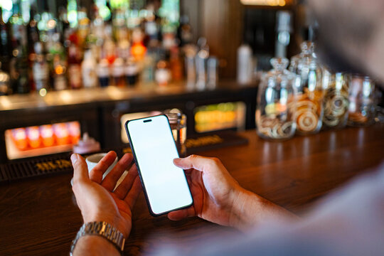 Person's hands using smartphone with white screen at a restaurant bar counter