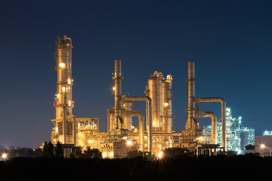 Illuminated petrochemical plant at Map Ta Phut, Rayong, Thailand, with process columns, interconnected pipes and steel platforms against dark blue night sky, highlighting industrial infrastructure.
