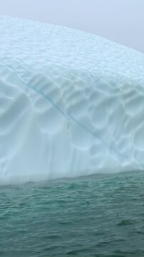 Vertical Video of Close Ice Edge and Textured Frozen Surface. White and blue ice, rippling water and soft diffuse light reveal natural frozen texture and sculpted contours across the marine scene.