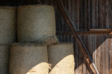 Round hay bales stacked in wooden barn with light and shadow © SWMedia