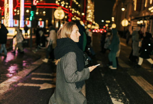 Woman Walks Across Street in City During Nighttime Holiday Season