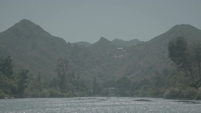 Layered mountain ridges and trees above a dry riverbed under a pale sky