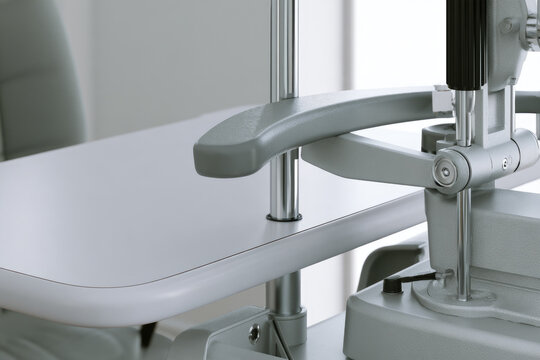 Optometry slit lamp examination unit with curved ergonomic chin rest and vertical illumination column on clean clinical desk beside window
