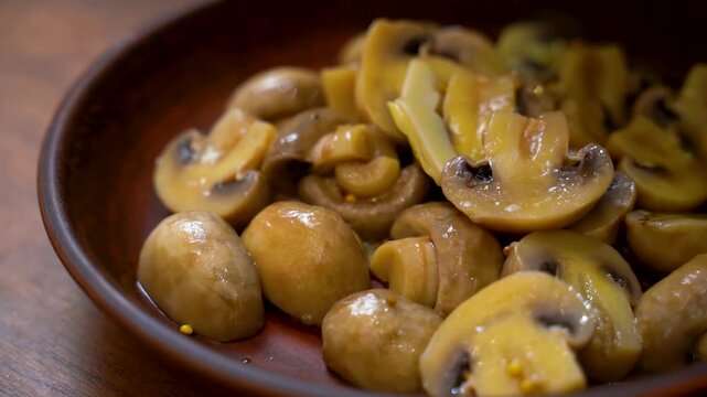 Putting marinated champignon mushrooms into a clay bowl
