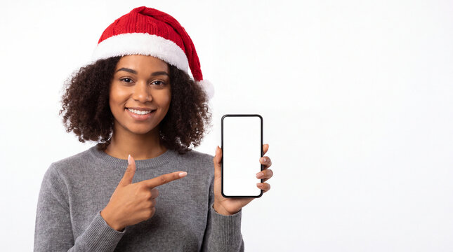 Smiling woman in Santa hat pointing at blank smartphone screen with one hand against white background, Christmas holiday portrait and mobile device mock up