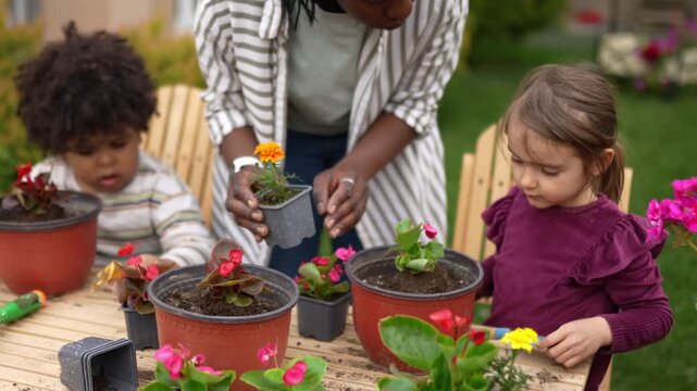 African American mother teaching her two multiracial children how to plant flowers in pots outdoors