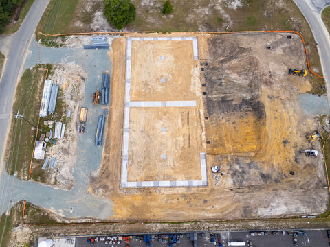 Aerial view of a new concrete foundation at a construction site with building materials and heavy machinery in Leland, North Carolina, United States.