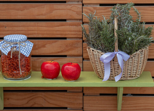 Rustic wicker basket with fresh rosemary, red apples, and jar of pasta on a wooden shelf