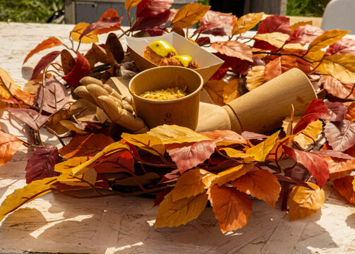 Autumn themed food display with wooden mannequin hands and paper cups among colorful artificial leaves