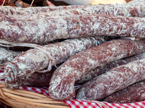 Close up of traditional dry cured salami sausages displayed in a wicker basket on a red checkered cloth