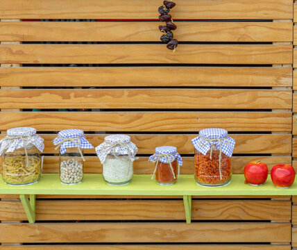 Glass storage jars filled with pasta, grains, and legumes arranged on a wooden shelf in a kitchen setting