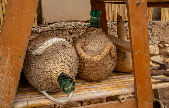 Vintage glass carboys wrapped in woven wicker casing beneath wooden structure