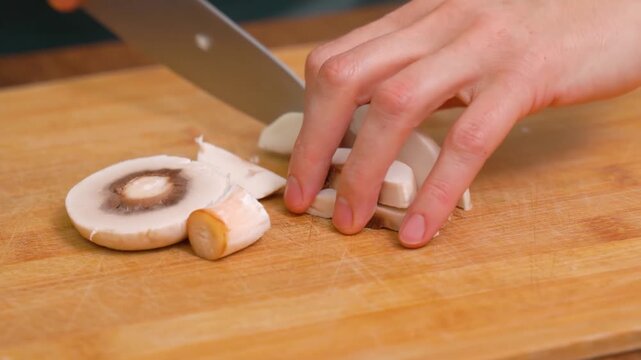 Cutting fresh champignon mushrooms with a knife on a cutting board