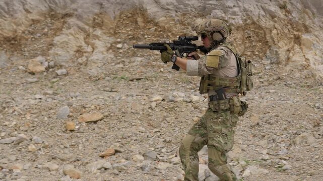 A special forces operator in full combat gear advances cautiously through a rocky, hostile environment while aiming his assault rifle on a tactical security patrol.