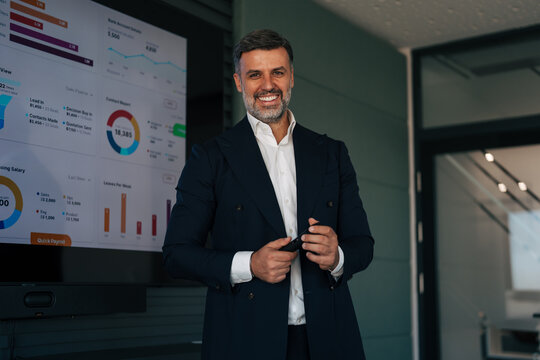 Confident businessman standing in modern office with data screen