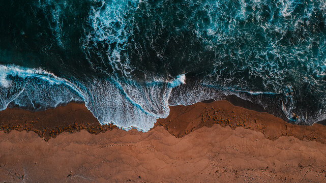 Aerial view of a sandy beach with turquoise waves crashing against the shore in Aimere, East Nusa Tenggara, Indonesia.