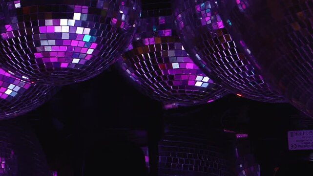 Mirrored Disco Balls Glow With Purple and Red Light. Reflective spheres fill the dark interior while tiled mirror surfaces scatter changing light into colorful abstract patterns.