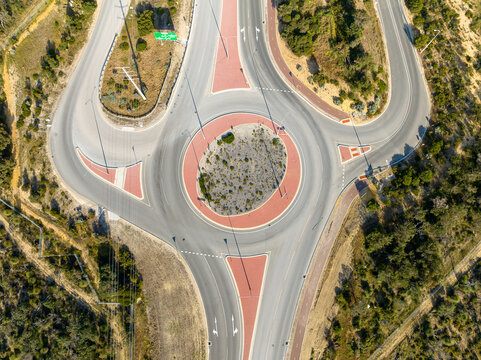 Aerial view of the Hester Avenue roundabout with red-painted traffic islands and surrounding native vegetation in Merriwa, Western Australia, Australia.