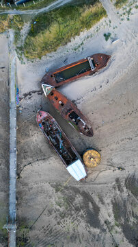 Aerial view of the rusted shipwrecks resting on the sandy beach next to the historic Instow Pier in Instow, Devon, United Kingdom.