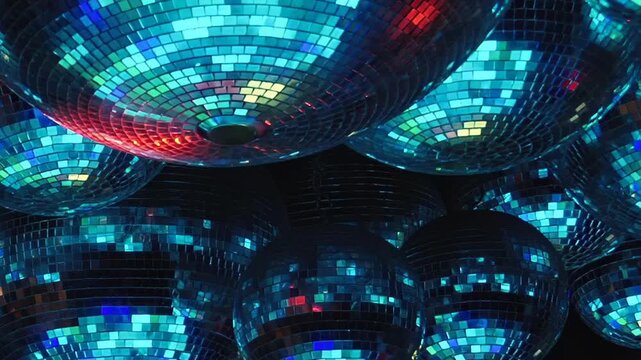 Green and Blue Reflections Across Mirrored Disco Balls. Mirrored mosaic surfaces catch changing colored light, creating shimmering patterns across the dark interior and rounded forms.