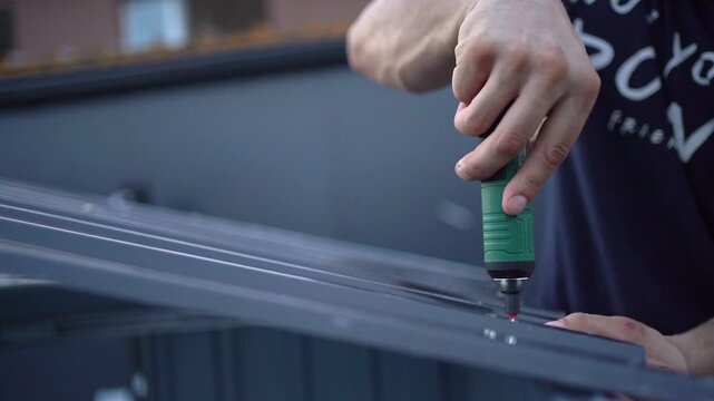 Man's hands using an electric screwdriver to assemble a metal structure in slow motion