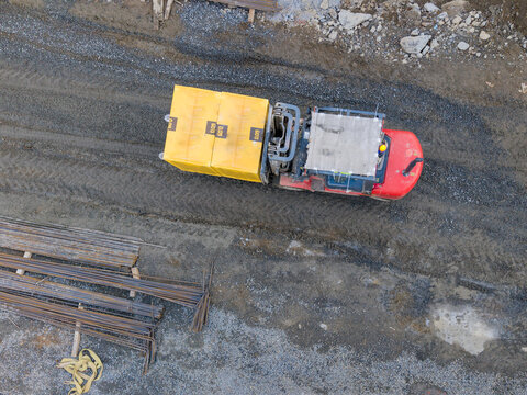 Aerial view of a forklift transporting yellow construction blocks on a gravel site with bundles of steel rebar nearby in Istanbul, Istanbul, Turkiye.