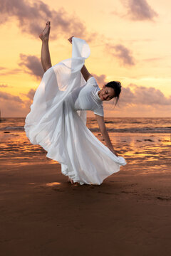 Young girl in white clothing doing tilt or side extension or grand battement pose at the beach during sunset at Kota Kinabalu beach Sabah Borneo
