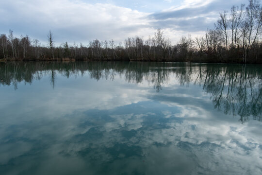 Cloud reflections on a still lake surrounded by bare trees