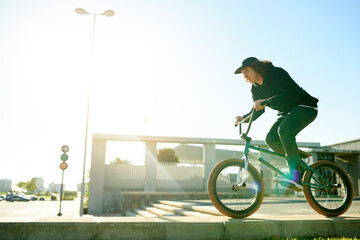 Naklejka premium BMX, man and bicycle in city for sports, urban challenge and exercise with space. Person, riding bike and cyclist on curb outdoor for fitness, extreme cycling and balance for stunt with flare