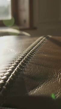 Vertical video: Camera pulling back tracking brown leather at home, showing stitch to reveal grain