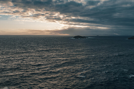 Aerial view of the dramatic Southern Ocean at sunset with dark, moody clouds and a small island visible in the distance near The Gap in Torndirrup, Western Australia, Australia.