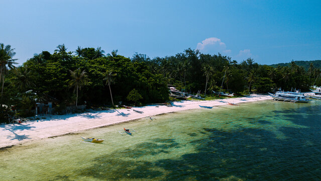 Aerial view of Boracay Island with outrigger boats anchored along the white sand beach, surrounded by lush tropical trees and turquoise waters in Malay, Western Visayas, Philippines.