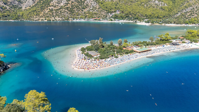 Aerial view of the famous Oludeniz Blue Lagoon with its turquoise waters, sandy beach, sun loungers, and surrounding pine-covered mountains in Oludeniz, Mugla, Turkiye.