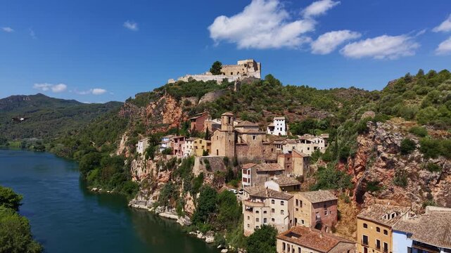 Aerial view of Miravet, a medieval hilltop village in Tarragona, Catalonia, Spain, featuring the Templar castle ruins atop rocky cliffs overlooking the green Ebro River