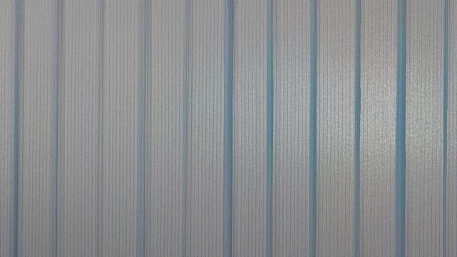 Abstract texture of a modern jalousie or shutters on building facade with vertical lines. Shifting light and shadow create a subtle and minimalist graphic pattern