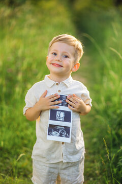 Smiling little boy holding ultrasound photos for a family pregnancy announcement in nature