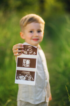 Young boy holding ultrasound photos in park celebrating baby sibling announcement and family joy