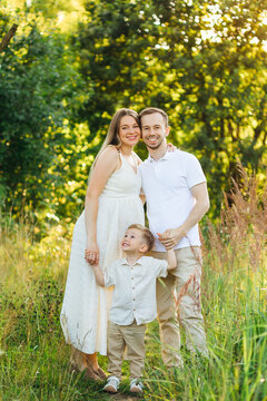Happy family portrait of parents with young son holding hands in sunlit meadow