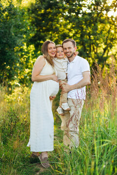 Pregnant family portrait with parents and young son smiling in a sunlit summer field